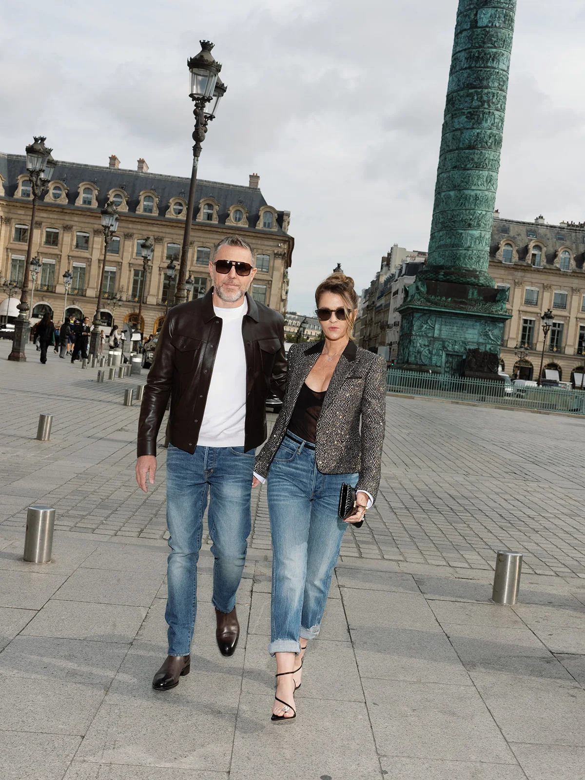 Couple wearing Tom Ford denim and jackets walking beside the Vendôme Column in Paris