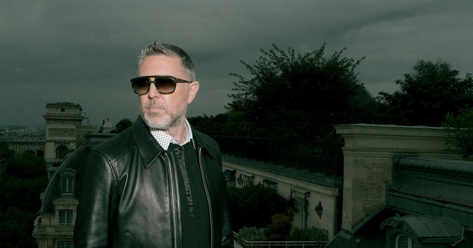 Man in a black leather jacket on a Paris rooftop with the Arc de Triomphe in the background