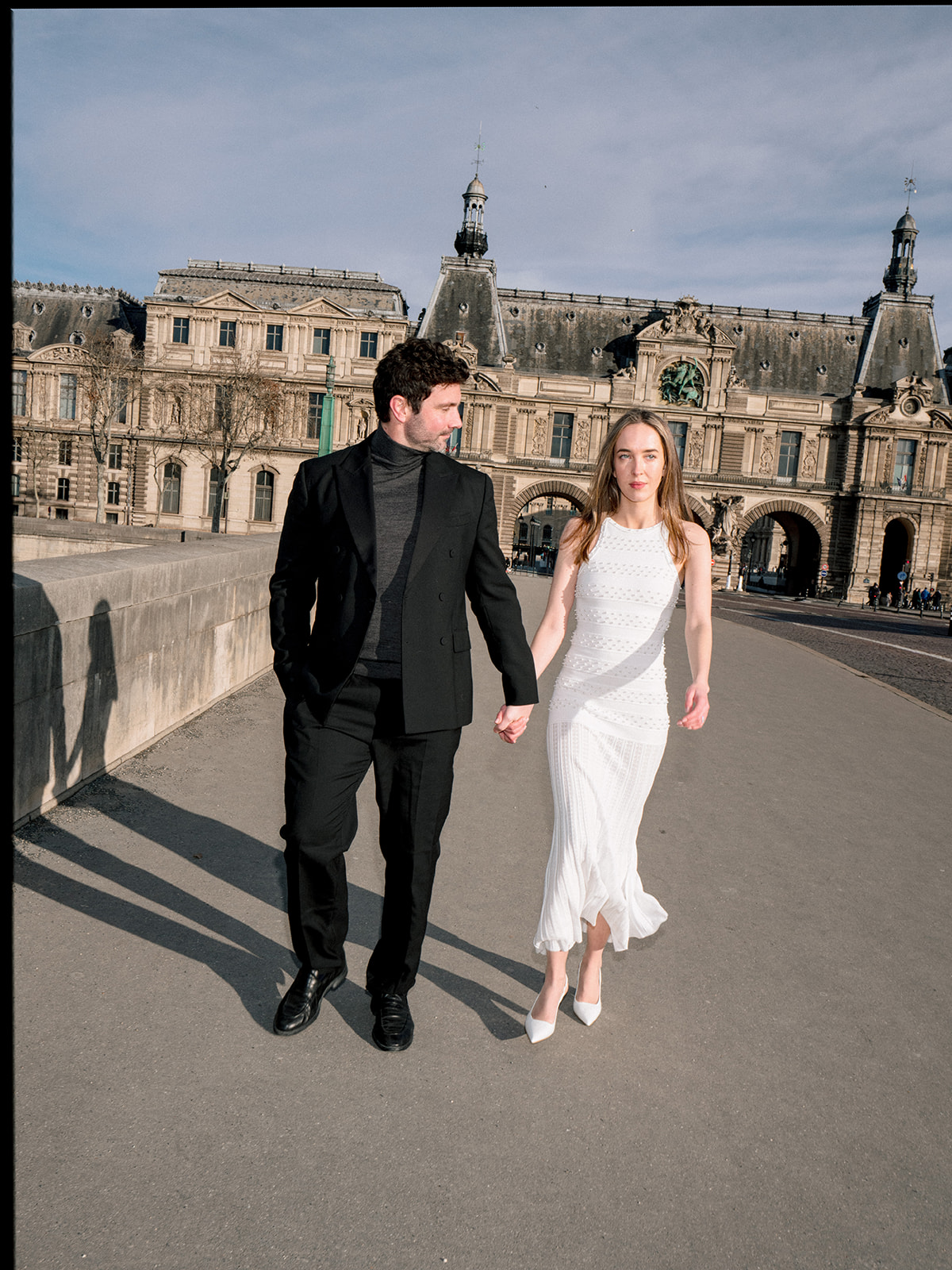 Fashion-forward couple walking hand in hand in front of the Louvre Museum in Paris