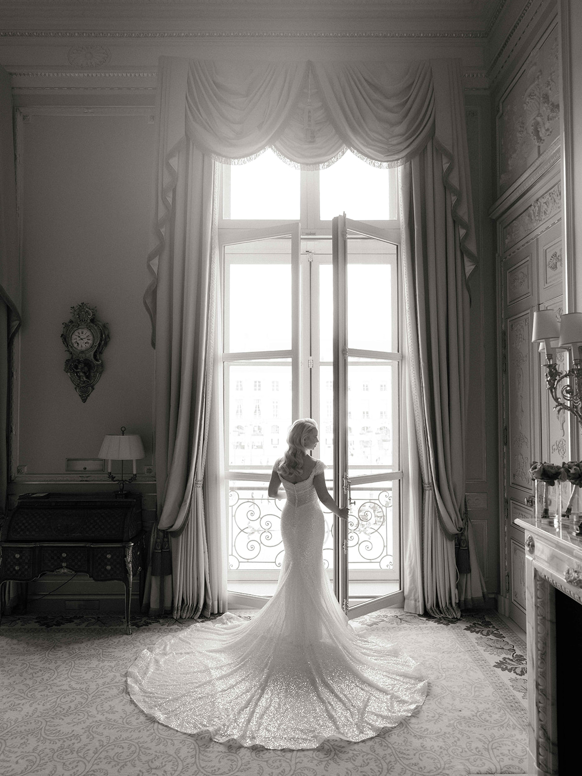 Portrait en noir et blanc de la mariée devant les fenêtres de sa suite au Ritz Paris