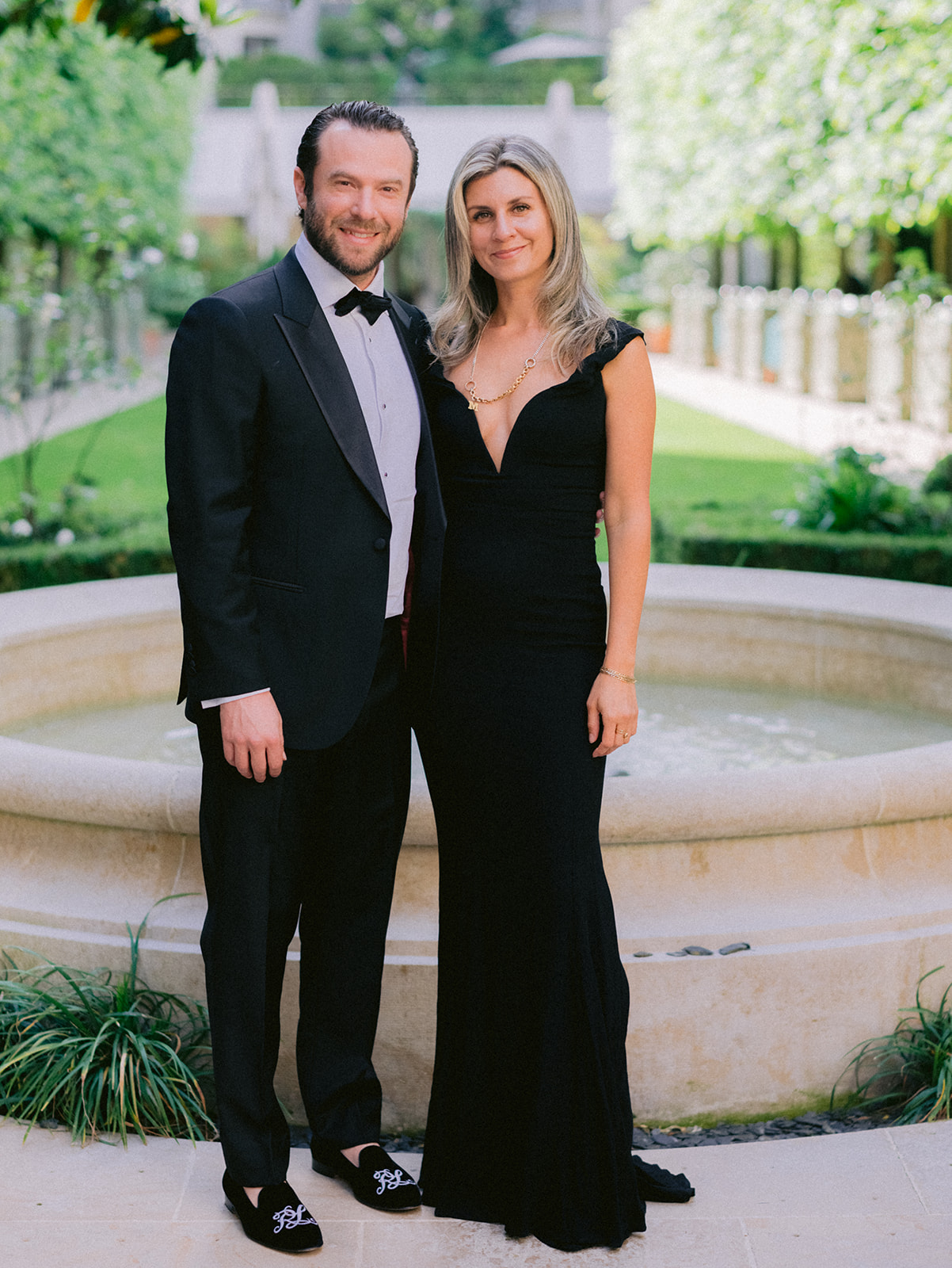 Black-tie wedding guests posing beside a fountain in a Paris garden