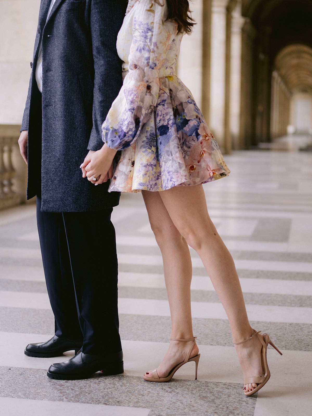 Fashion detail of a couple holding hands beneath the Louvre arcades in Paris