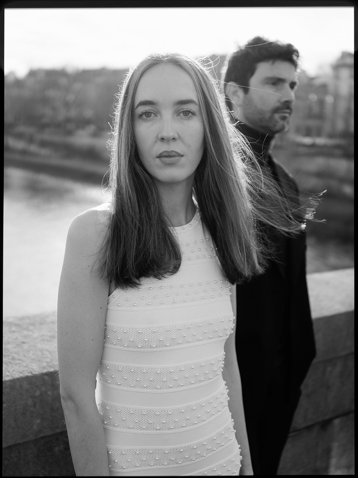 Black-and-white editorial couple portrait with the woman in focus beside the Seine