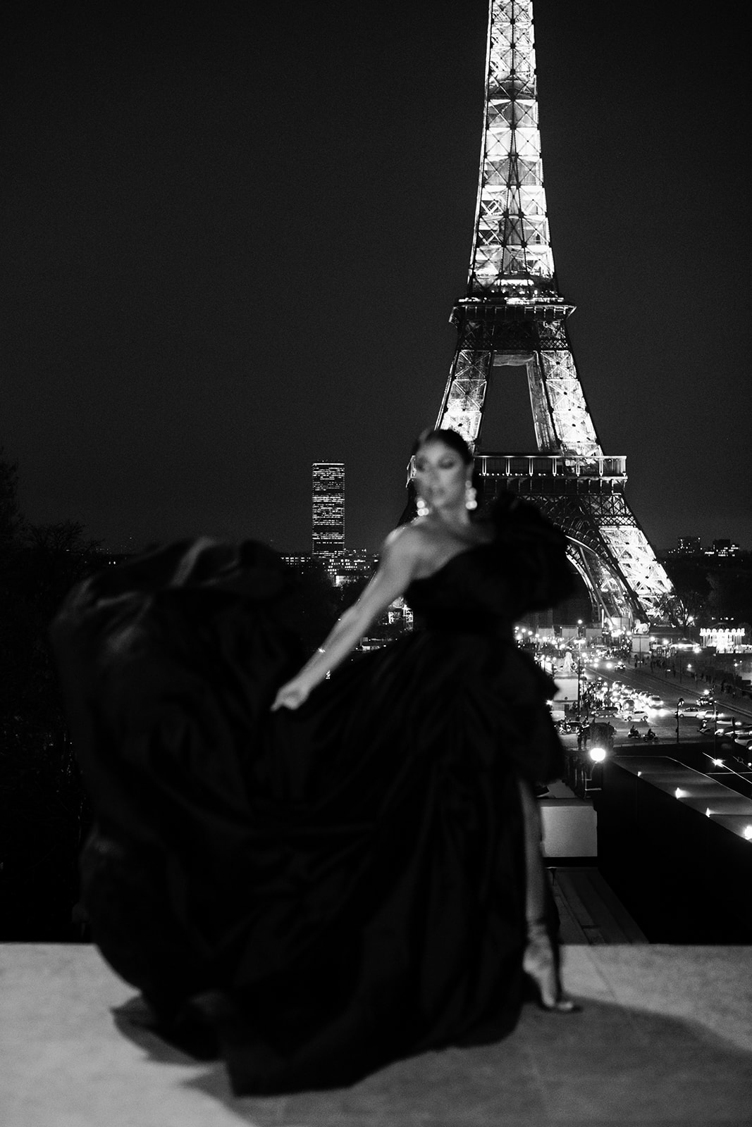 Candice Craig posing in a dramatic black gown at night in front of the Eiffel Tower