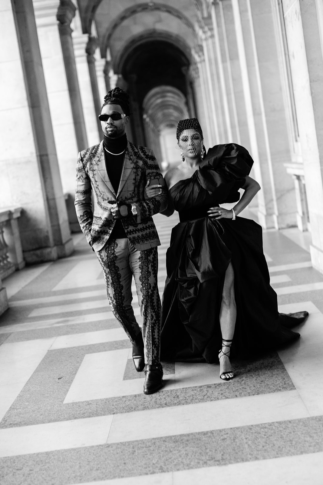 Candice Craig and Omar Bolden photographed in formal fashion looks beneath the Louvre arcades in Paris