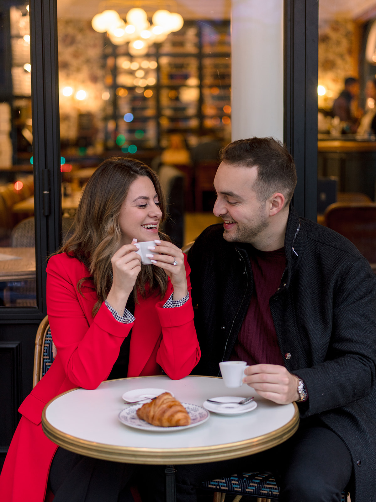 American couple laughing over coffee and a croissant during their Paris photoshoot