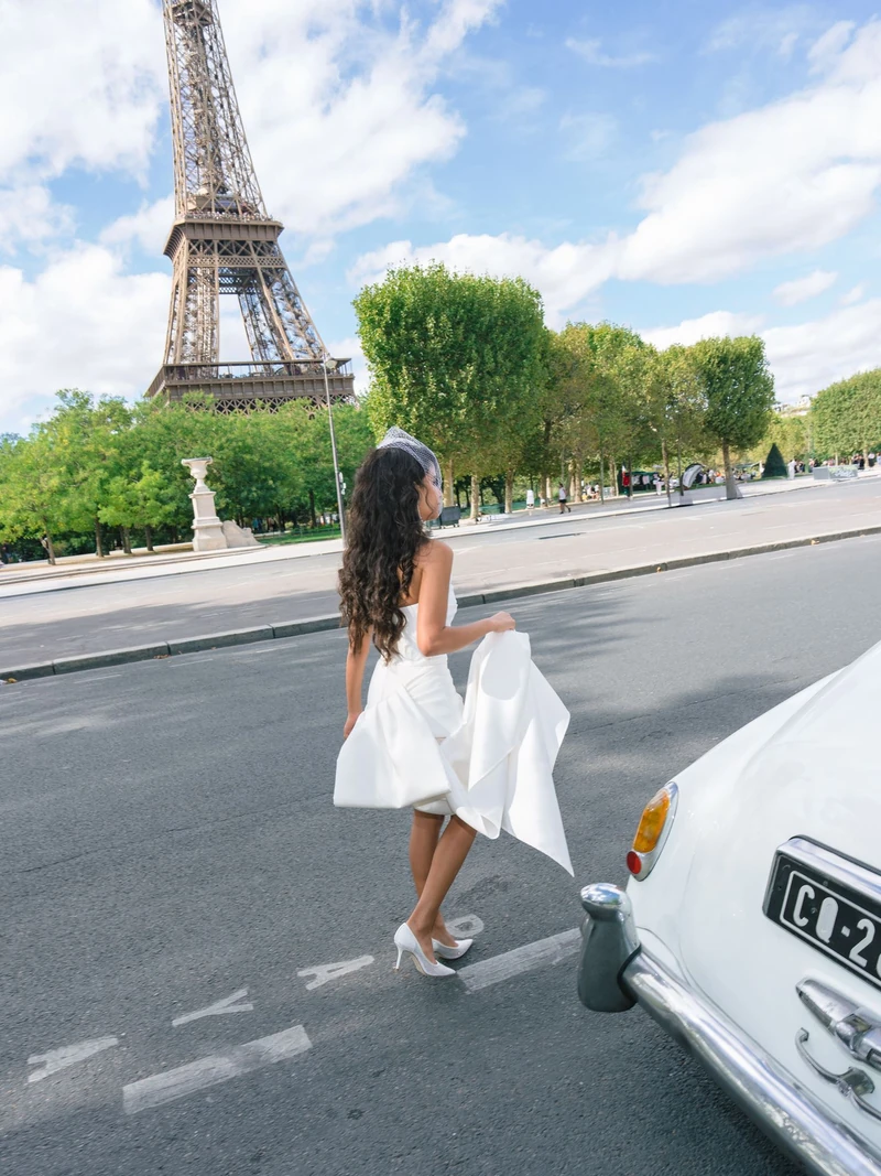 Bride walking beside a white car with the Eiffel Tower behind her during a two-day Paris wedding