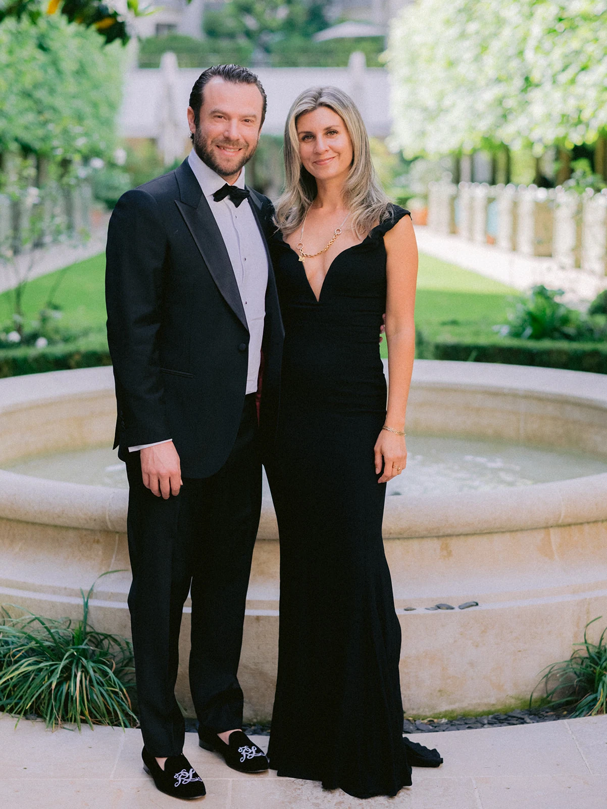 Black-tie wedding guests posing beside a fountain in a Paris garden
