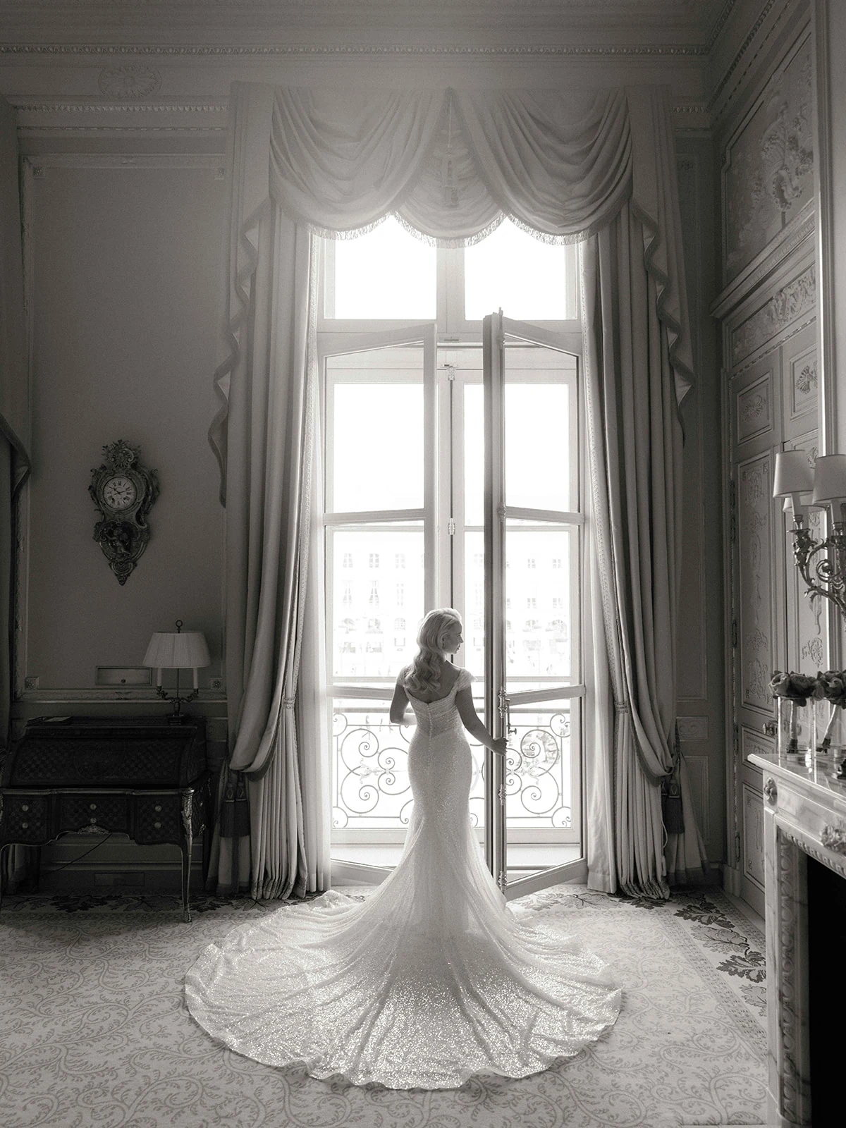 Portrait en noir et blanc de la mariée devant les fenêtres de sa suite au Ritz Paris
